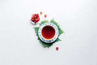 A cup of tea sits on a leaf with a white background