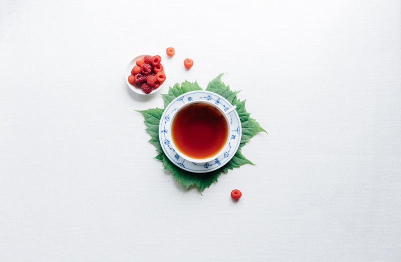 A cup of tea sits on a leaf with a white background