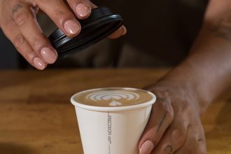 Hand places lid on a Detpak Precision Series takeaway coffee cup