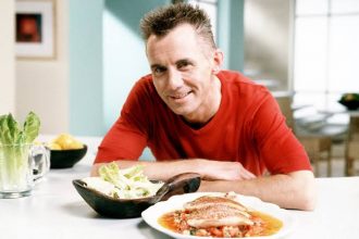 Gary Rhodes smiling at camera with plate of food in front of him