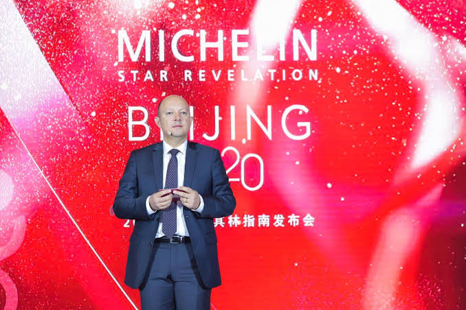 Man in a grey suit standing infront of red screen with text saying michelin