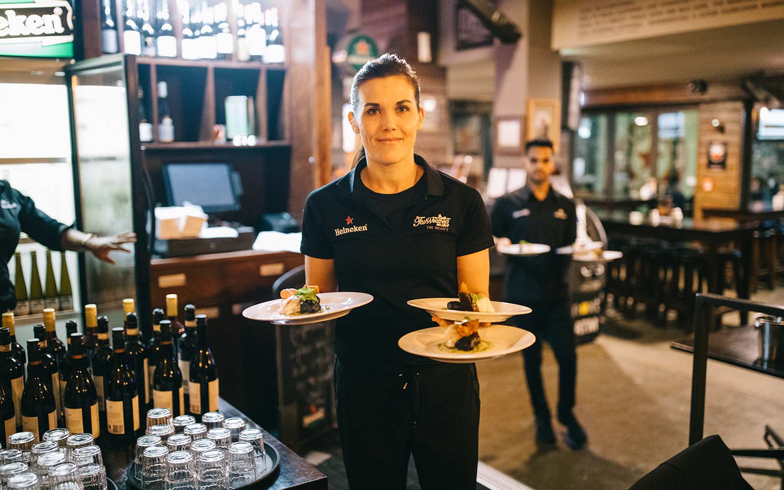 Female waiter looking at camera holding three plates of food