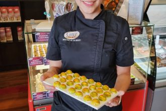 female baker chef standing in uniform holding a tray of sweets, smiling