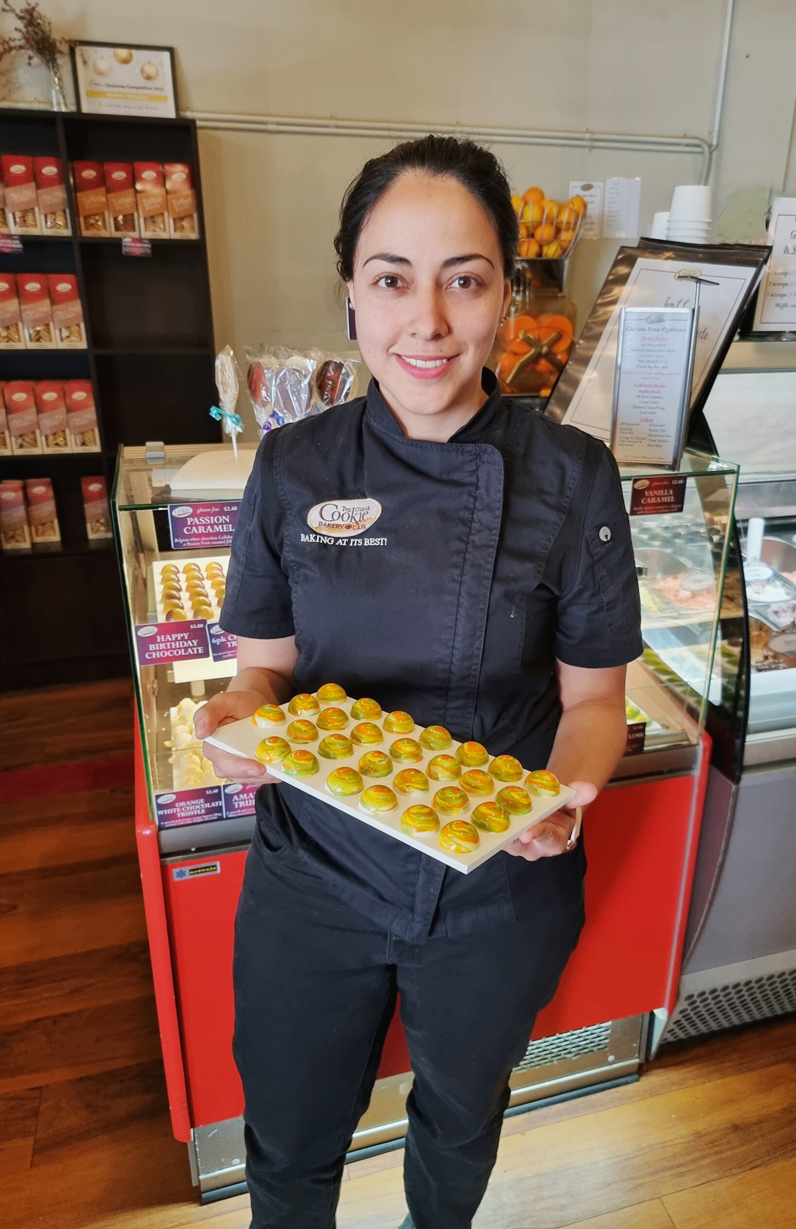 female baker chef standing in uniform holding a tray of sweets, smiling