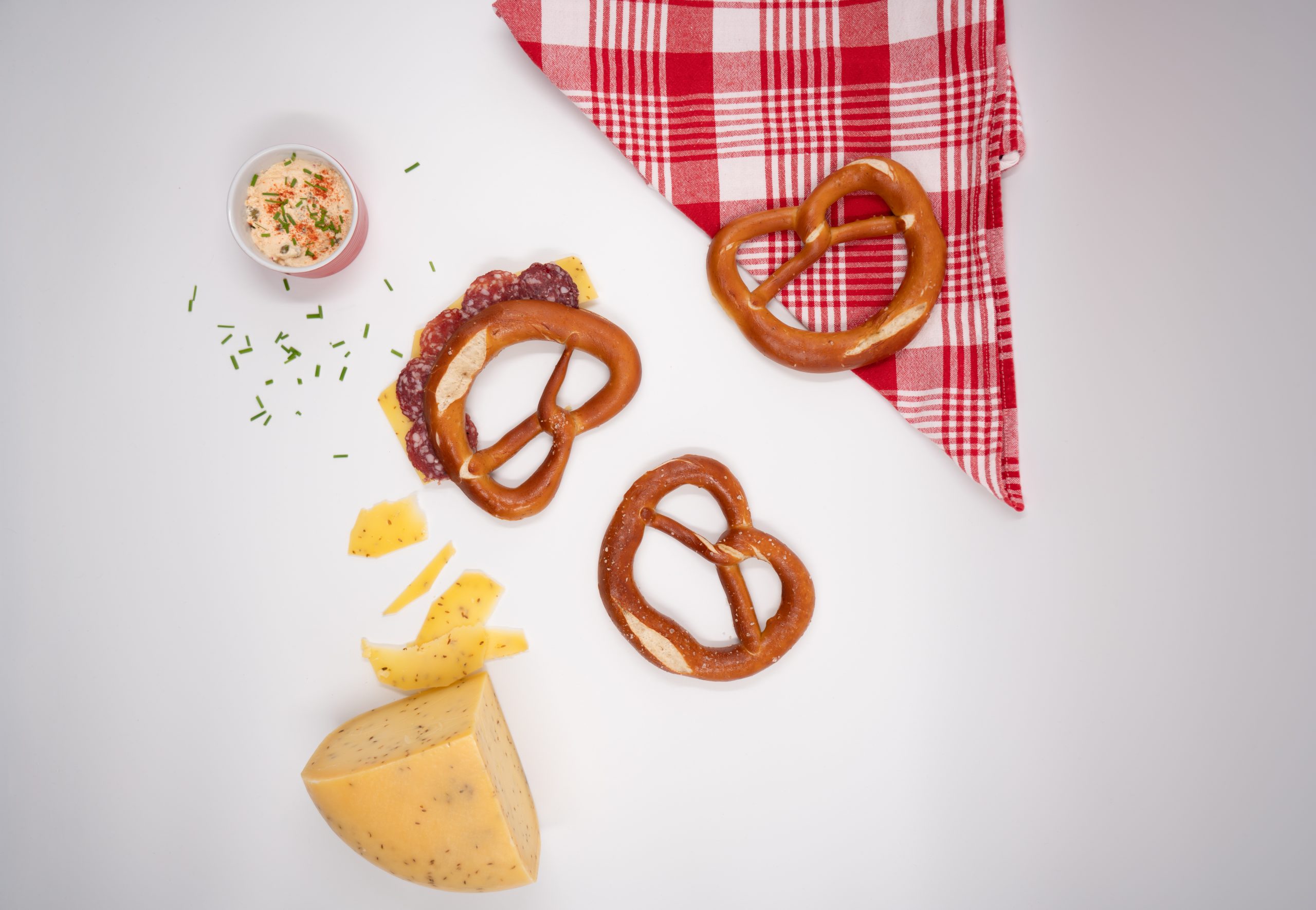 dough pretzels on white background with a block of cheese and red tartan cloth