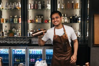 Male bartender smilking and holding drink mixer behind bar