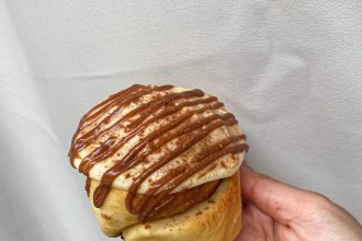 cinnamon bun held in hand with sauce drizzle